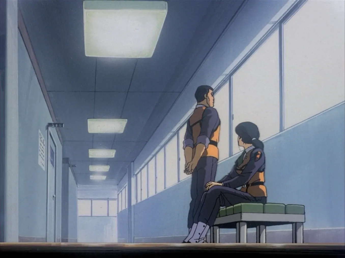 A still from Patlabor: Goto stands and Nagumo sits on a bench in a nondescript hallway.