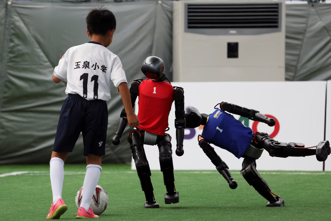 A human soccer player faces off against two robot players, one of which is falling over