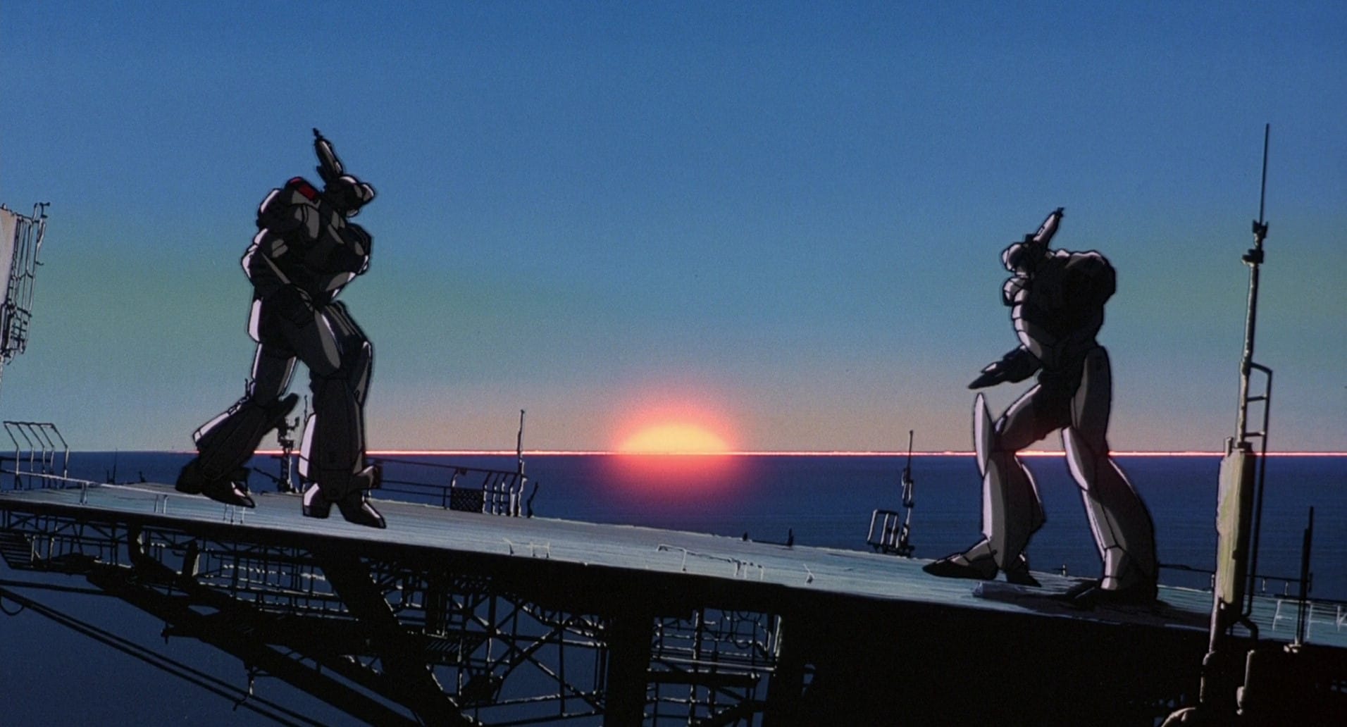 An image from the Patlabor anime, with two broken Patlabor's standing facing each other with an ocean sunrise in the background.