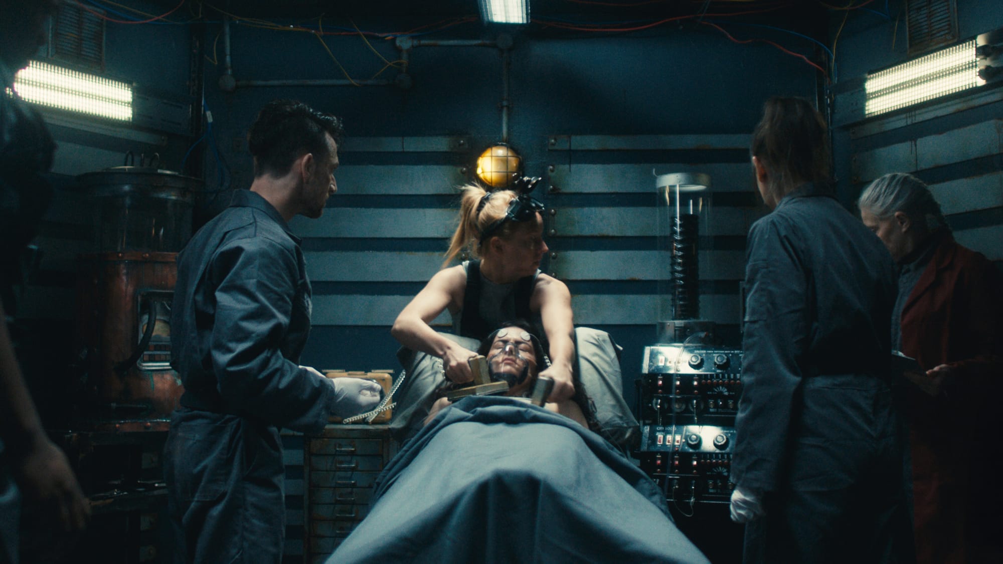  A group of people gather around a woman on a surgical table in Dead Reset, a FMV horror game set in a cramped facility with sinister secrets.