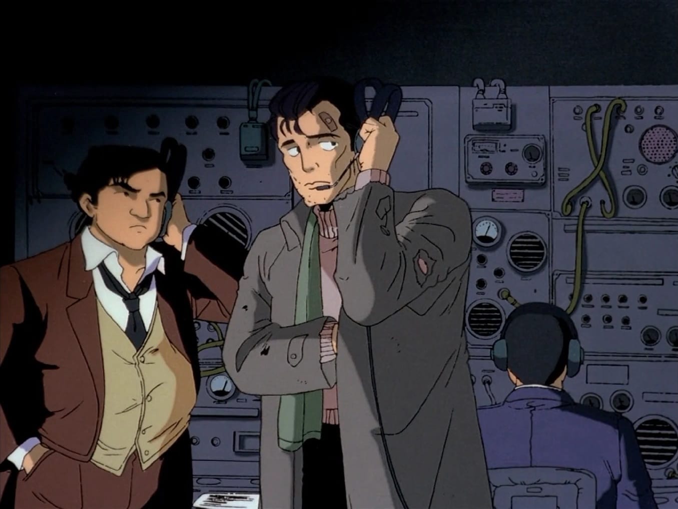 An image from the Patlabor anime depicting the character Goto in a disheveled state alongside Detective, both of whom are listening to headsets.